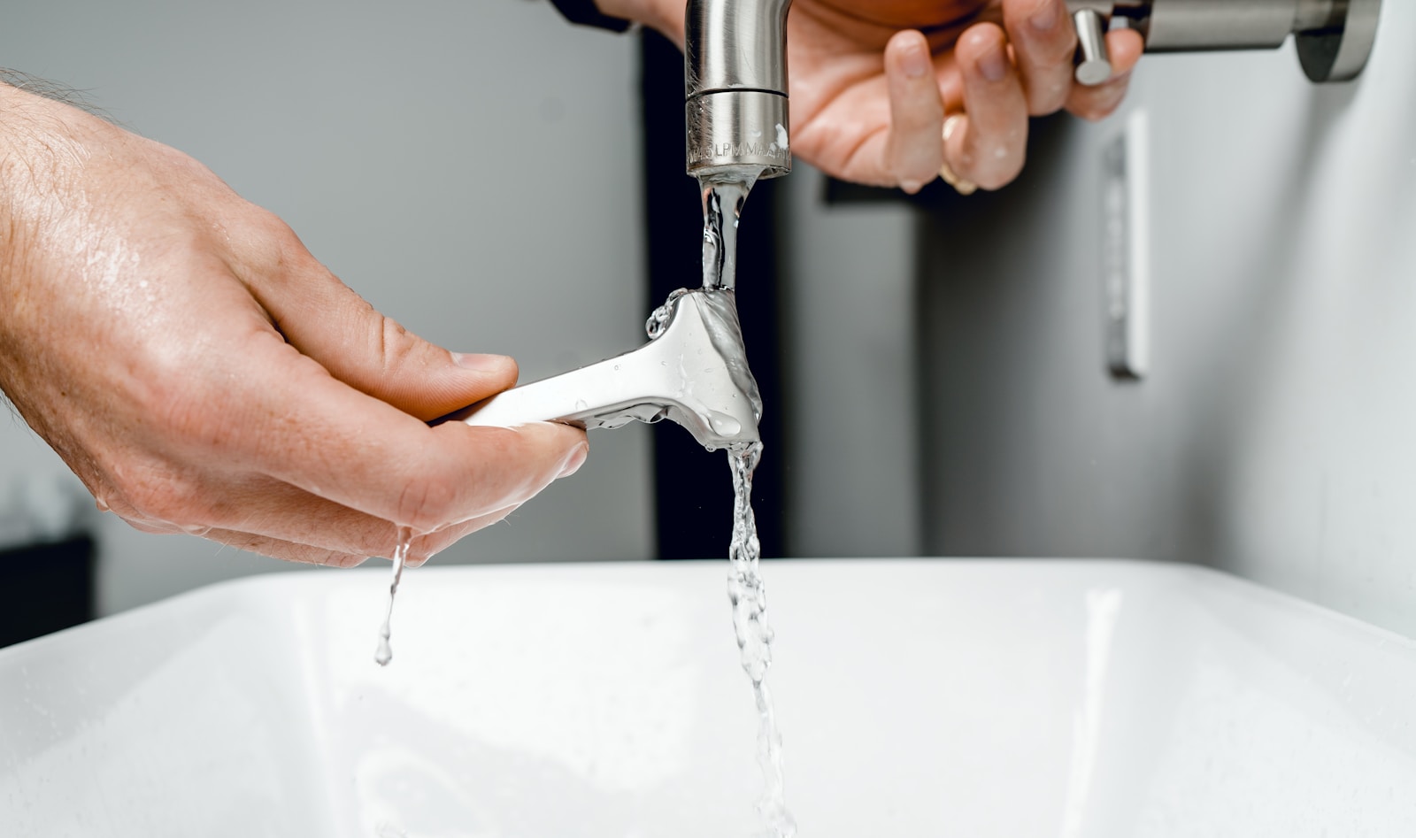 A hand holds a razor under flowing water from a faucet, demonstrating the process of rinsing before shaving. Context suggests grooming tips.